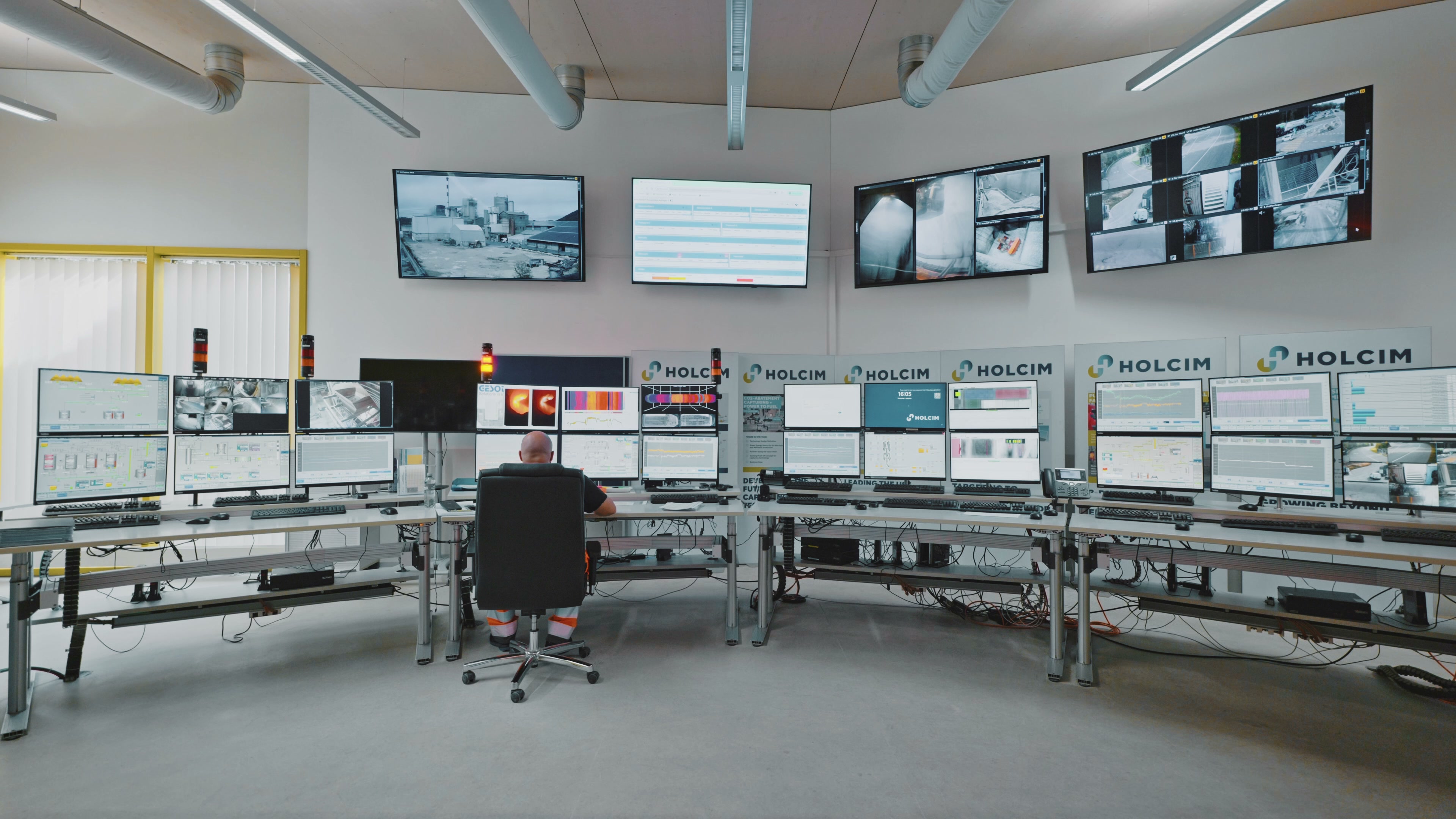 A Holcim operator working in the plant control room, surrounded by live process and camera displays