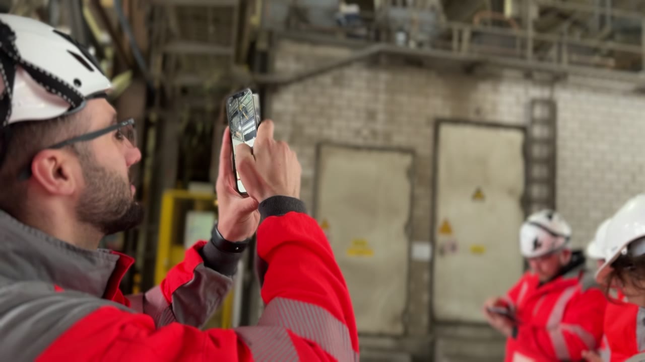 A team in protective equipment using phones in an industrial plant